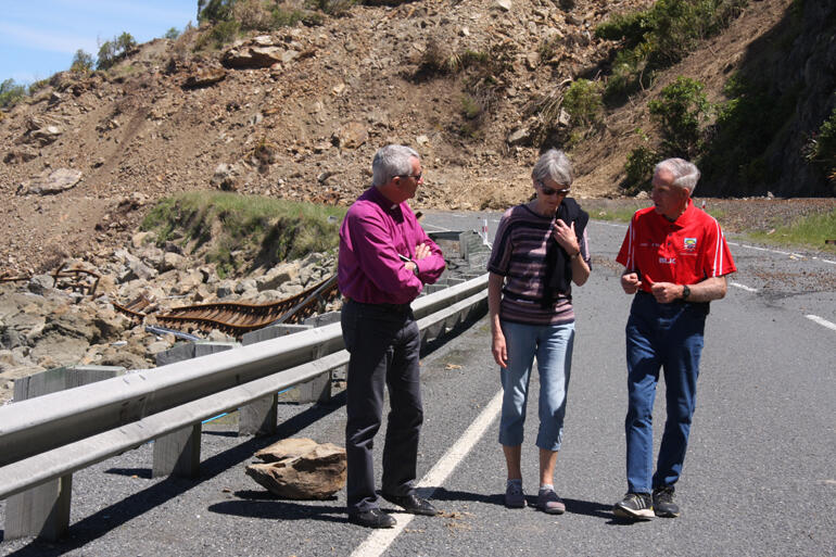 Bishop Richard and Hilary walk near the northernmost slip on State Highway One, as Malcolm explains the road closure's impact on farmers. 