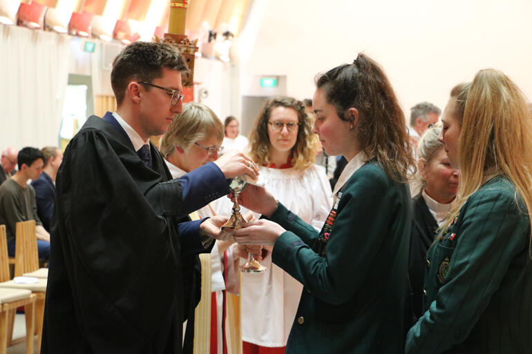 St Margaret's College students Hannah Langley and Virginia Macdonald receive the Eucharist from diocesan Vice Chancellor, Alex Summerlee. 
