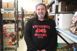 A bearded man in a woollen hat smiles as he stands among shelves of food