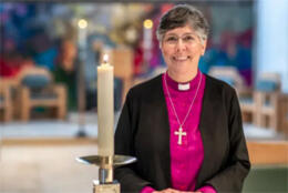 A grey-haired female Iranian Church of England bishop smiles in a Cathedral