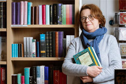 A woman holds a Bible in front of a bookshelf full of Bibles