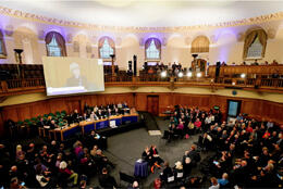 A large circular synod hall with rounded arches is filled with scores of delegates
