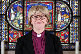 Bishop Sarah Mullally stands before a highly colored historic stained glass window