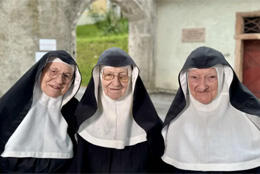 3 elderly nuns in wimples smile in historic stone courtyard
