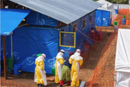 Medical workers clothed head to toe in protective plastic garments and head masks walk alongside a temporary medical tent hospital