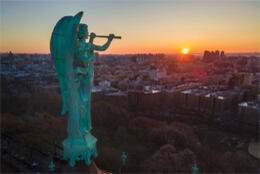 A pale green bronze angel blows a trumpet over the new York skyline as the sun rises