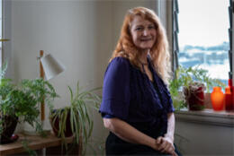 A middle aged female red haired psychologist stands in a light room with indoor plants