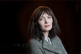 A middle aged woman with dark hair lit against a black background