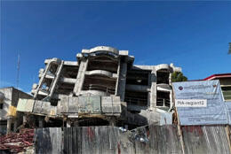 A concrete building falls half-collapsed against a blue sky