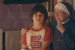 A young boy sits looking pensive next to a veiled Catholic nun