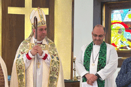 Middle aged male Palestinian Anglican Bishop speaks at a lectern, wearing a purple cassock