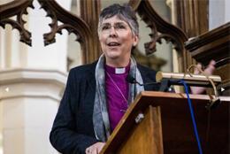 Middle aged Iranian Anglican female bishop preaches in a wooden pulpit