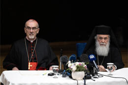 Roman Cardinal in black and red robe and Orthodox Archbishop in black robe, hat and veil