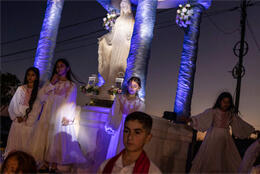Young girls in white dresses dance near a sculpture of Mary