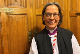A female bishop stands in the wooden stalls of the UK House of Lords: Bp Helen-Ann Hartley