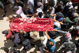 Dead body wrapped in red blankets is carried by a group of Palestinians