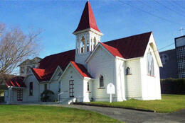 A white weatherboard church with a red roof bathed in sun against a blue sky