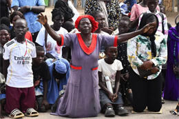 A Sudanese women kneels in a crowd with arms outstretched