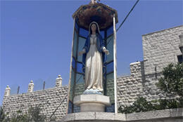 A plaster statue of Mary stands in an alcove on a sunbaked street