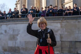 Archbishop of Canterbury Sarah Mullally waves from a road with pilgrim's staff and clergy collar