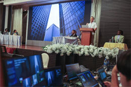 Four African women speakers listen while a European man speaks in front a projection of tall skyscrapers in a city financial district
