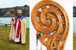 Bishop Richard stands in front of Akaroa harbour, koru-shaped carved wooden crozier studded with pounamu (green nephrite jade)