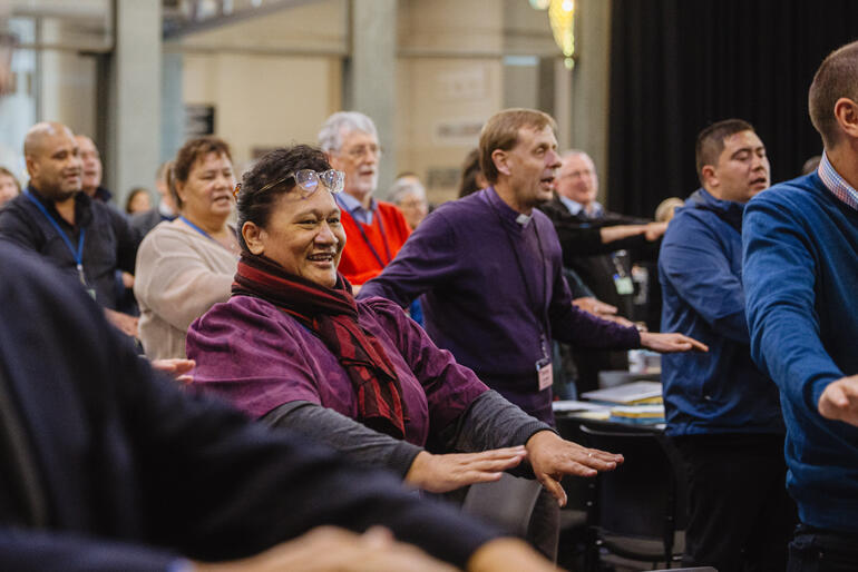 Synod members rise to sing 'Tutira mai ngā iwi' - 'Gather the people together'.