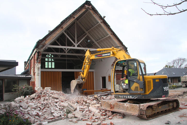 The excavator drags the fallen bricks of the Churchill Courts chapel into a pile, ready to be carted away.