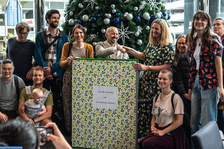 Members of Common Grace Aotearoa and advocates for better power company rules give a giant Xmas card to Electricity Authority CEO Sarah Gillies.